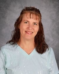 Portrait of a smiling person in a light blue blouse against a gray studio backdrop