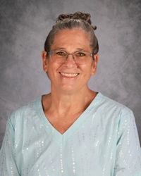 Smiling person in glasses wearing a light blue blouse against a gray studio backdrop