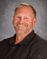 Smiling person in a black polo shirt against a gray studio backdrop