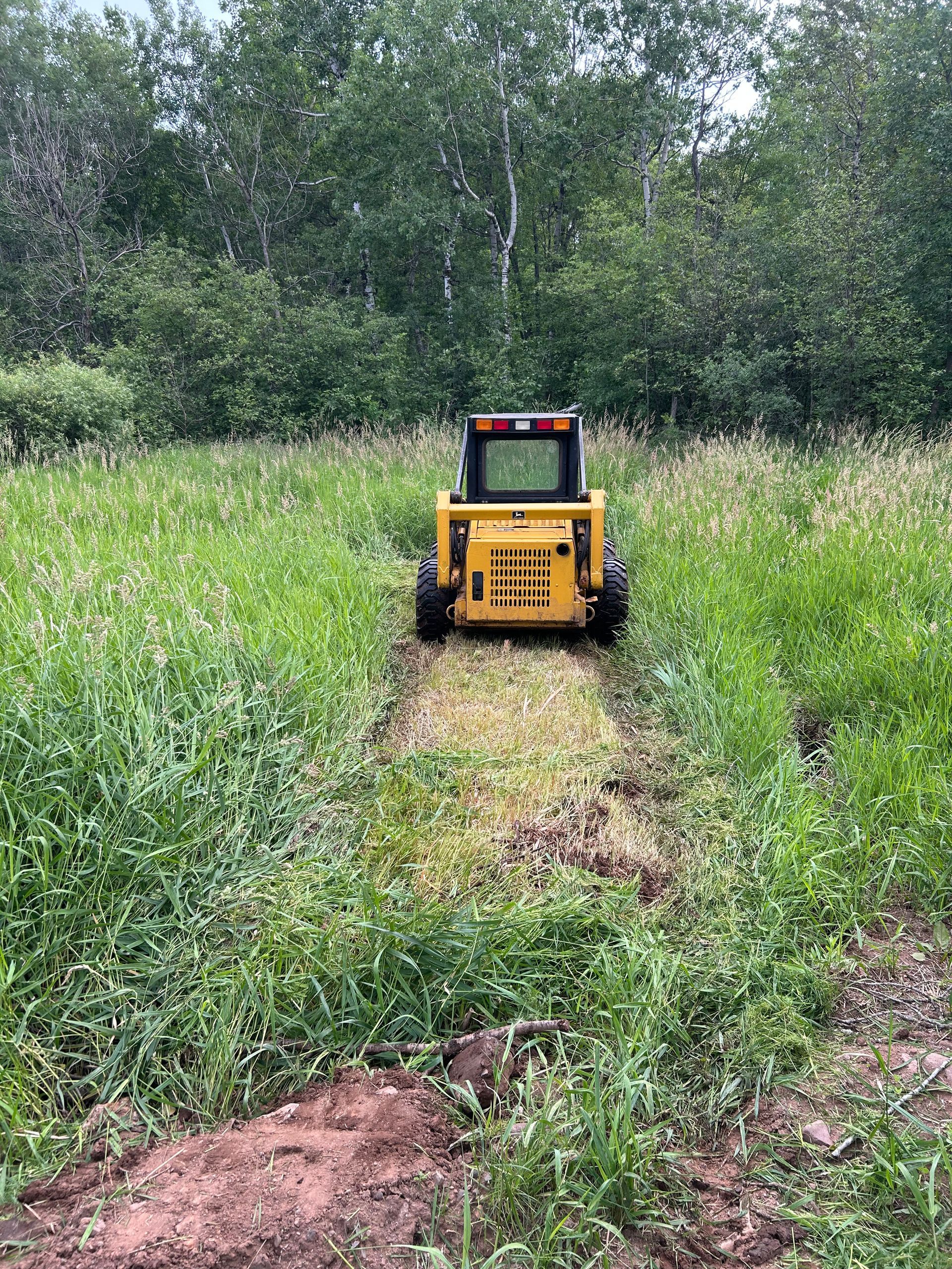 A yellow tractor is cutting grass in a field.