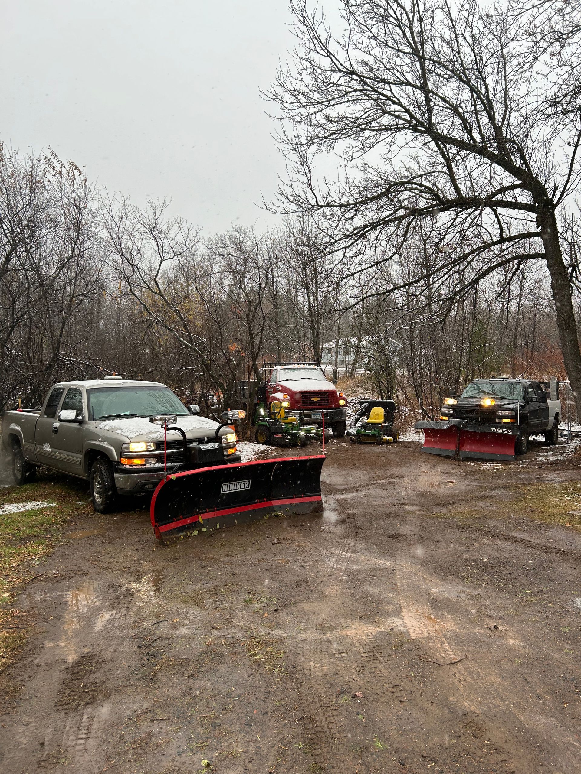 Two snow plows are parked on the side of a dirt road.