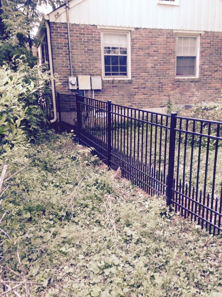 a black fence surrounds a lush green yard in front of a brick house .