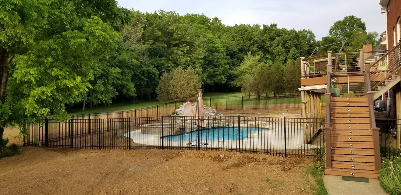 a large backyard with a fence and a swimming pool surrounded by trees .