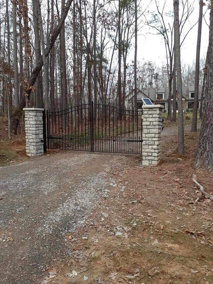 a driveway with a gate and pillars leading to a house in the woods .