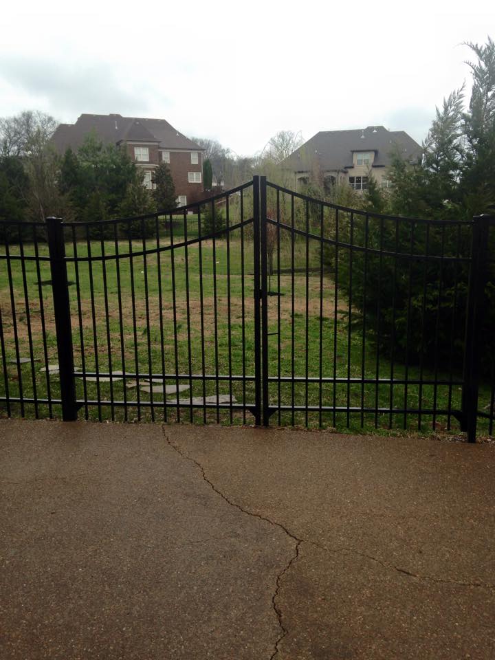 a black fence surrounds a grassy field with houses in the background