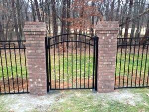 a black metal gate is surrounded by brick pillars and a fence .