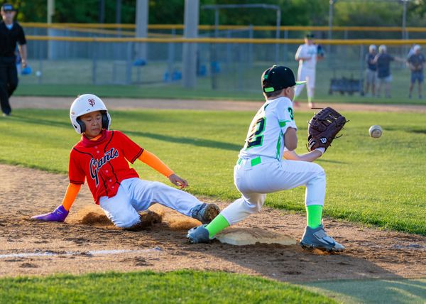 Youth baseball players sliding into base during a play on a sunny field