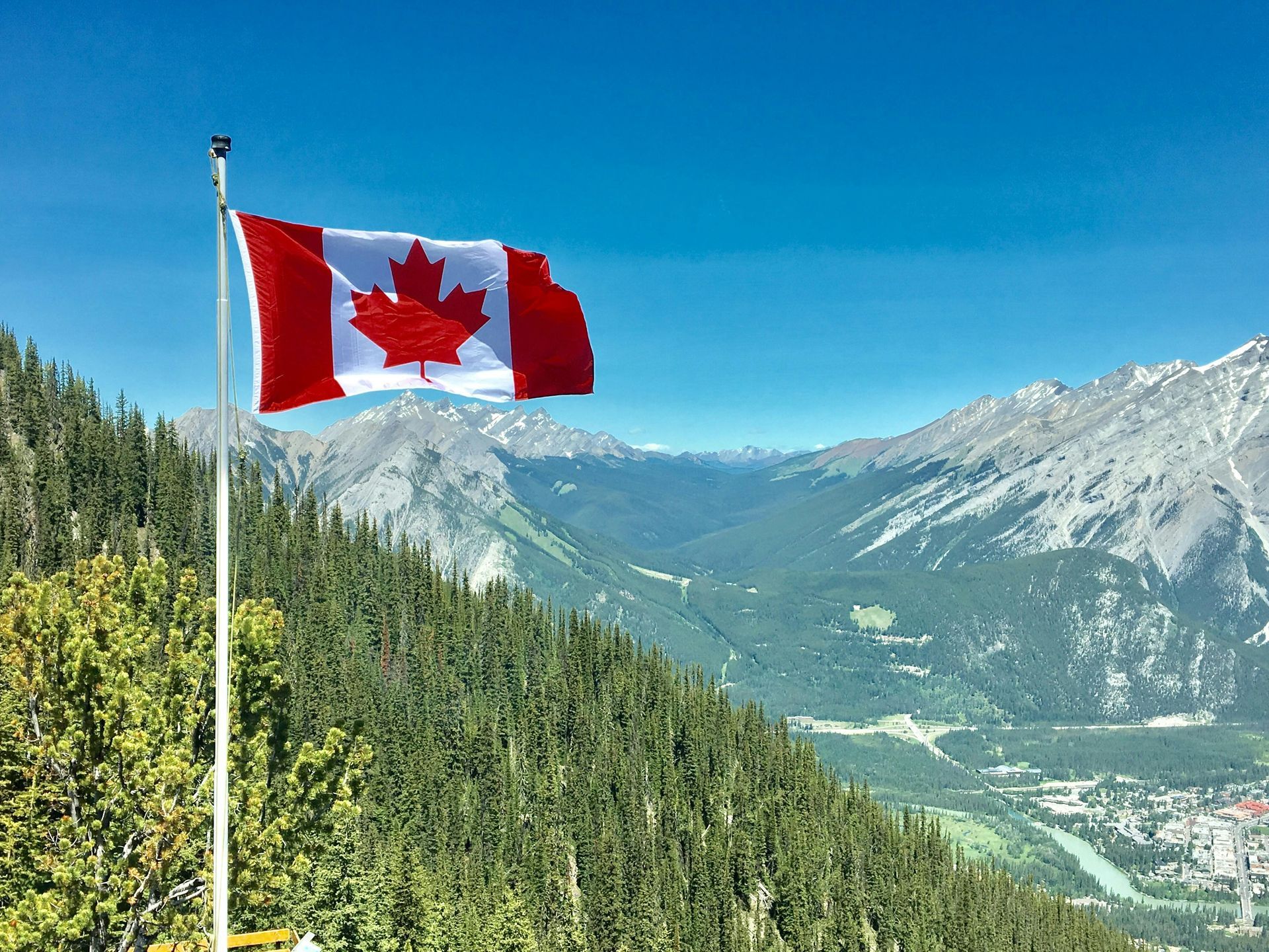 Canadian flag waving on a mountain overlooking a valley; sunny day.