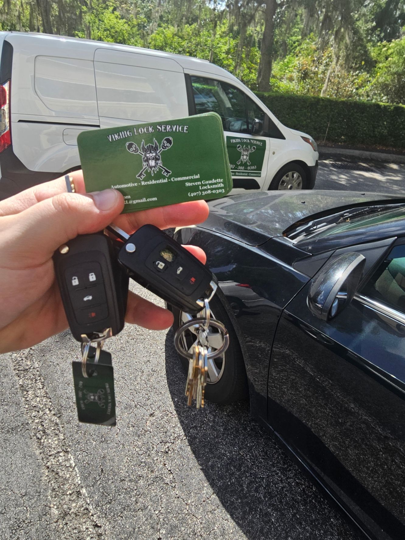 A person is holding a green card and keys in front of a car