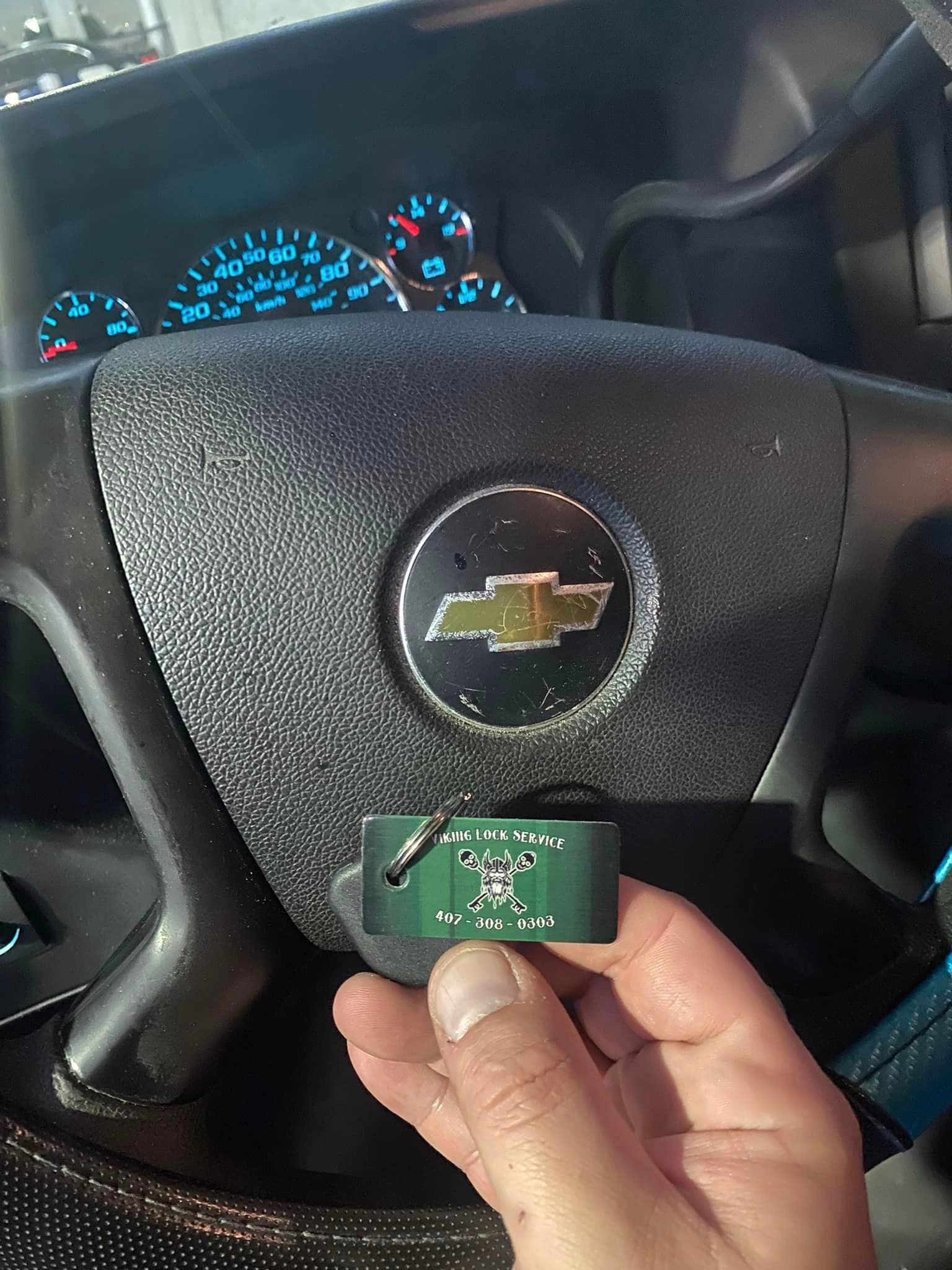 A person is holding a key in front of a chevrolet steering wheel.