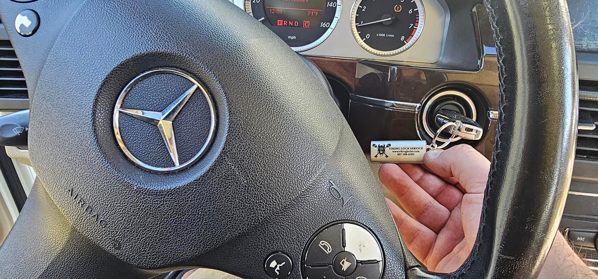 A person is holding a key in front of a mercedes steering wheel.
