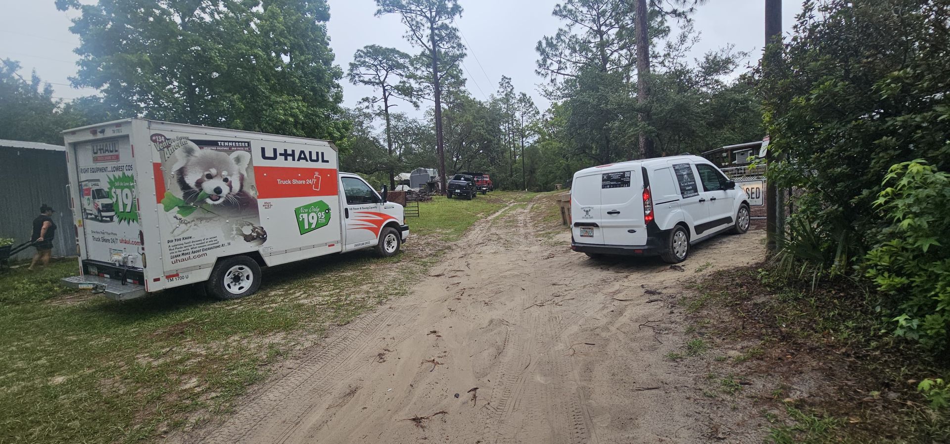 Two white vans are parked on the side of a dirt road.