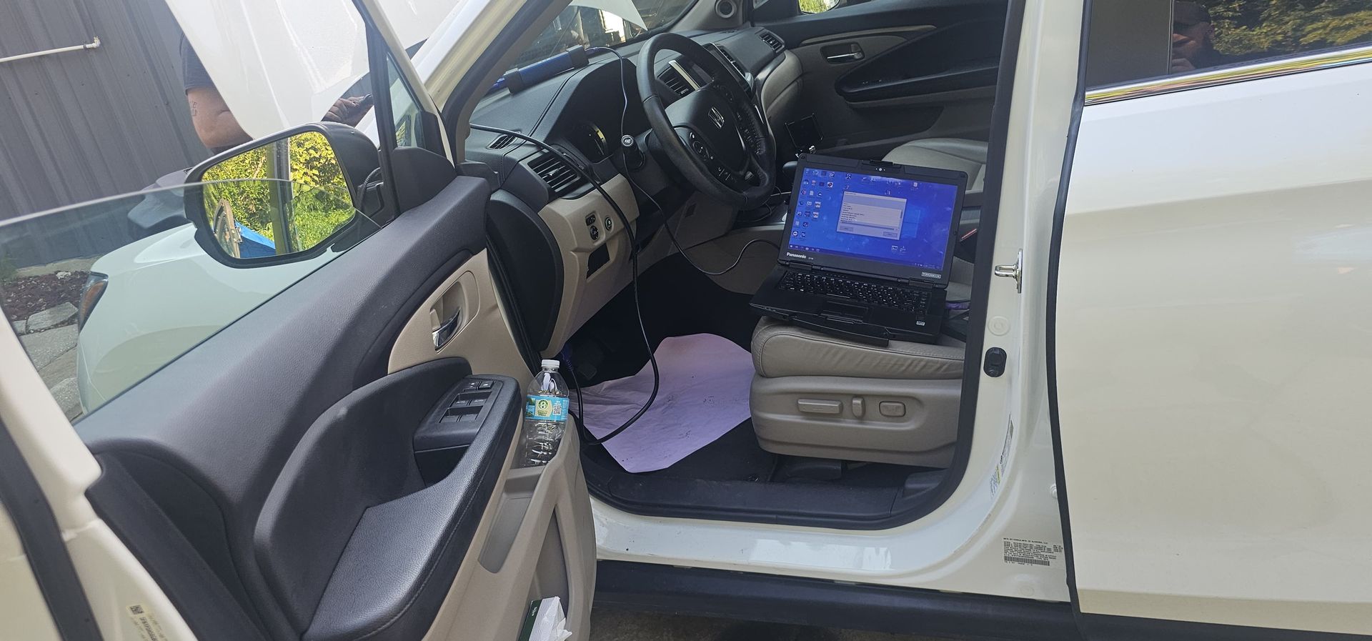 The inside of a white car with the door open and a laptop on the floor.