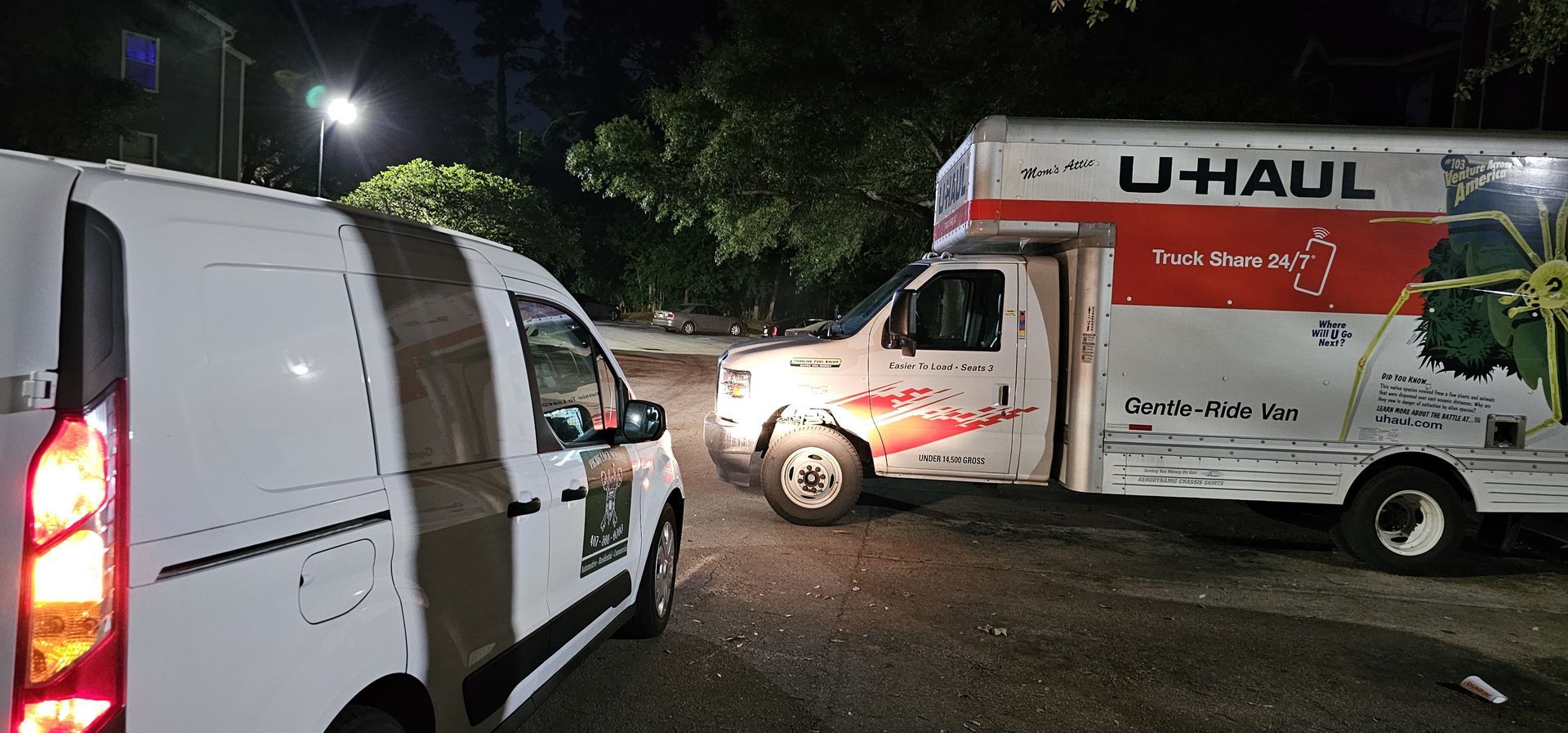 Two u-haul trucks are parked next to each other in a parking lot at night.
