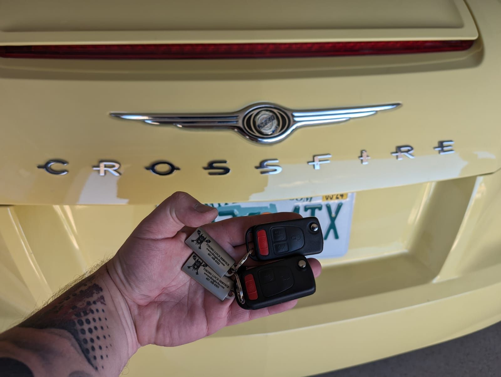 A person is holding a pair of keys in front of a yellow chrysler crossfire