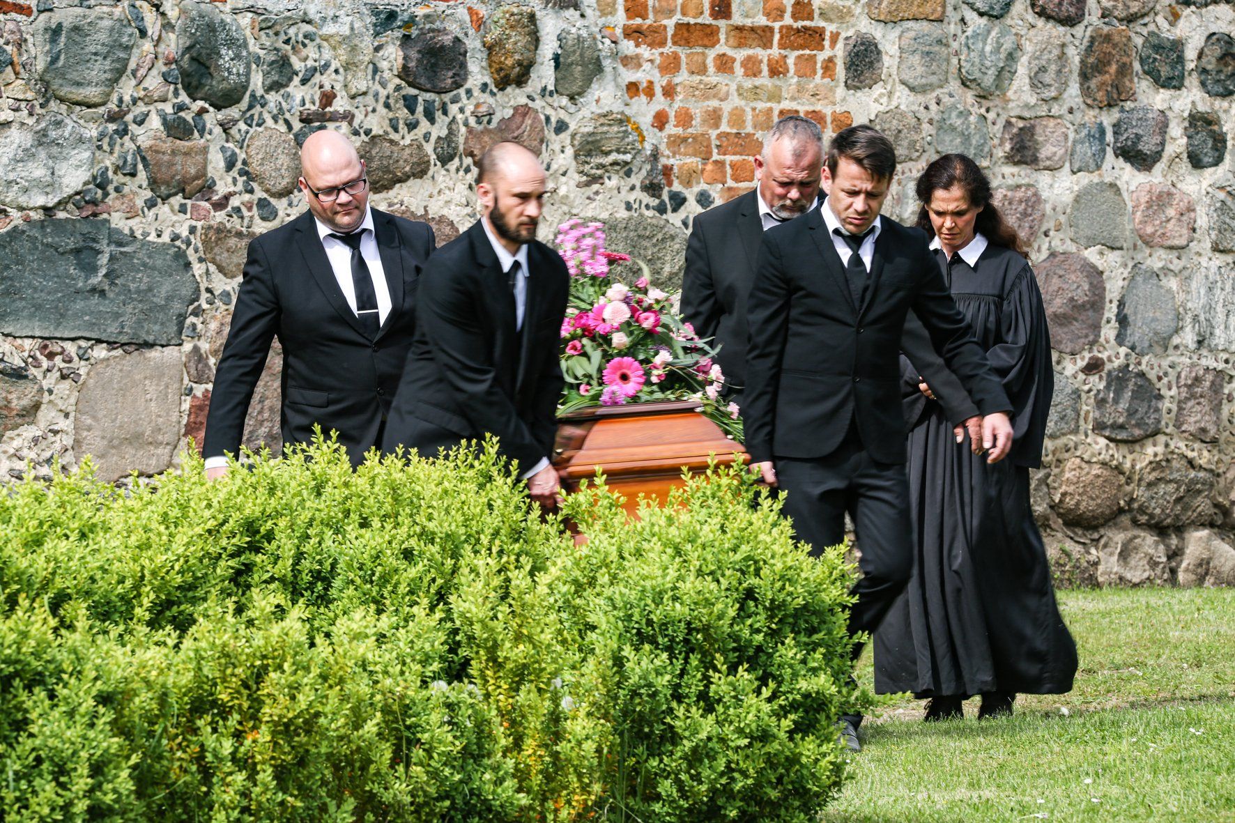 Eine Gruppe von Menschen in schwarzen Anzügen trägt einen Sarg