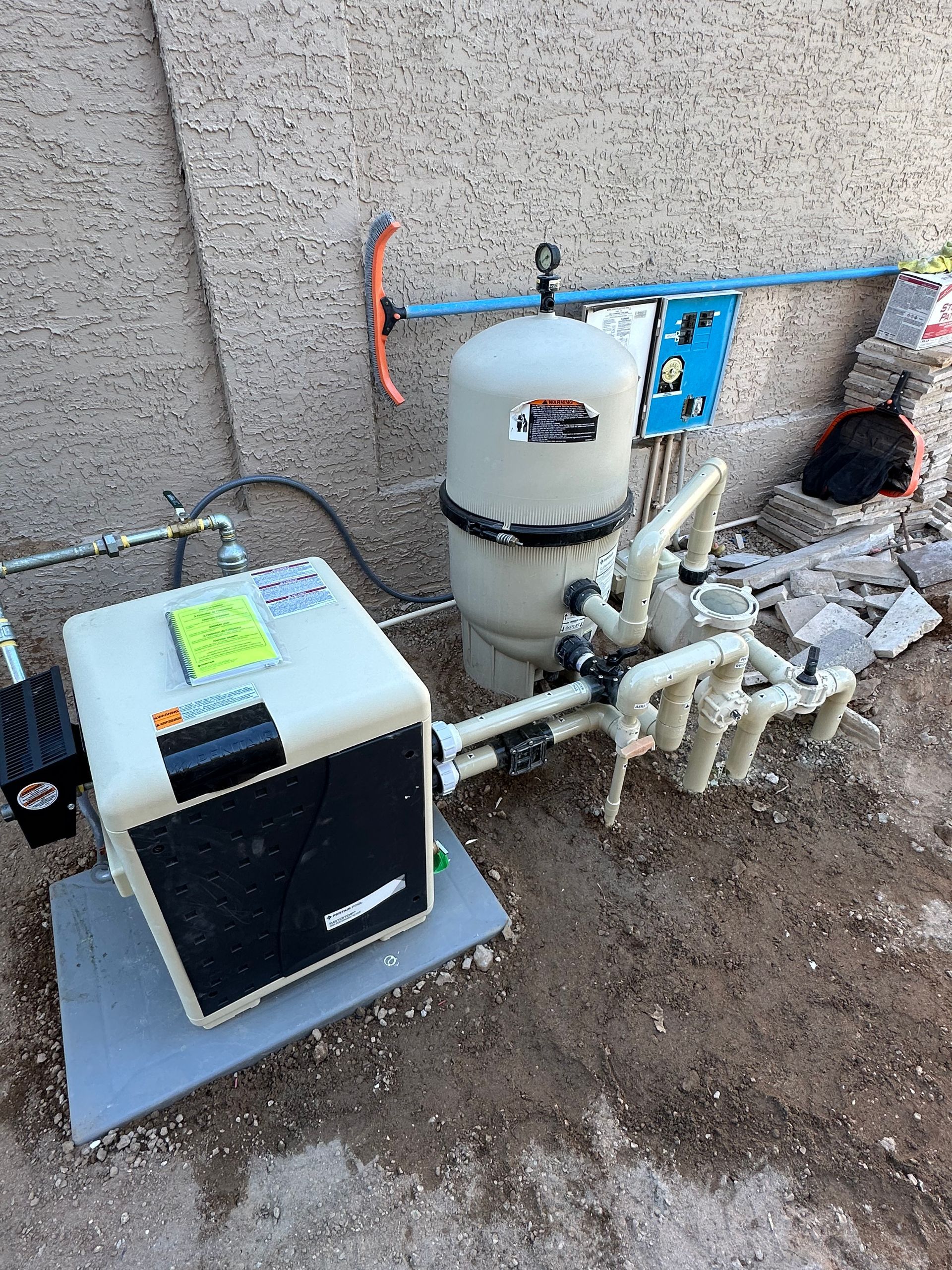 Pool equipment: heater, filter, and plumbing, set on a concrete pad next to a wall.