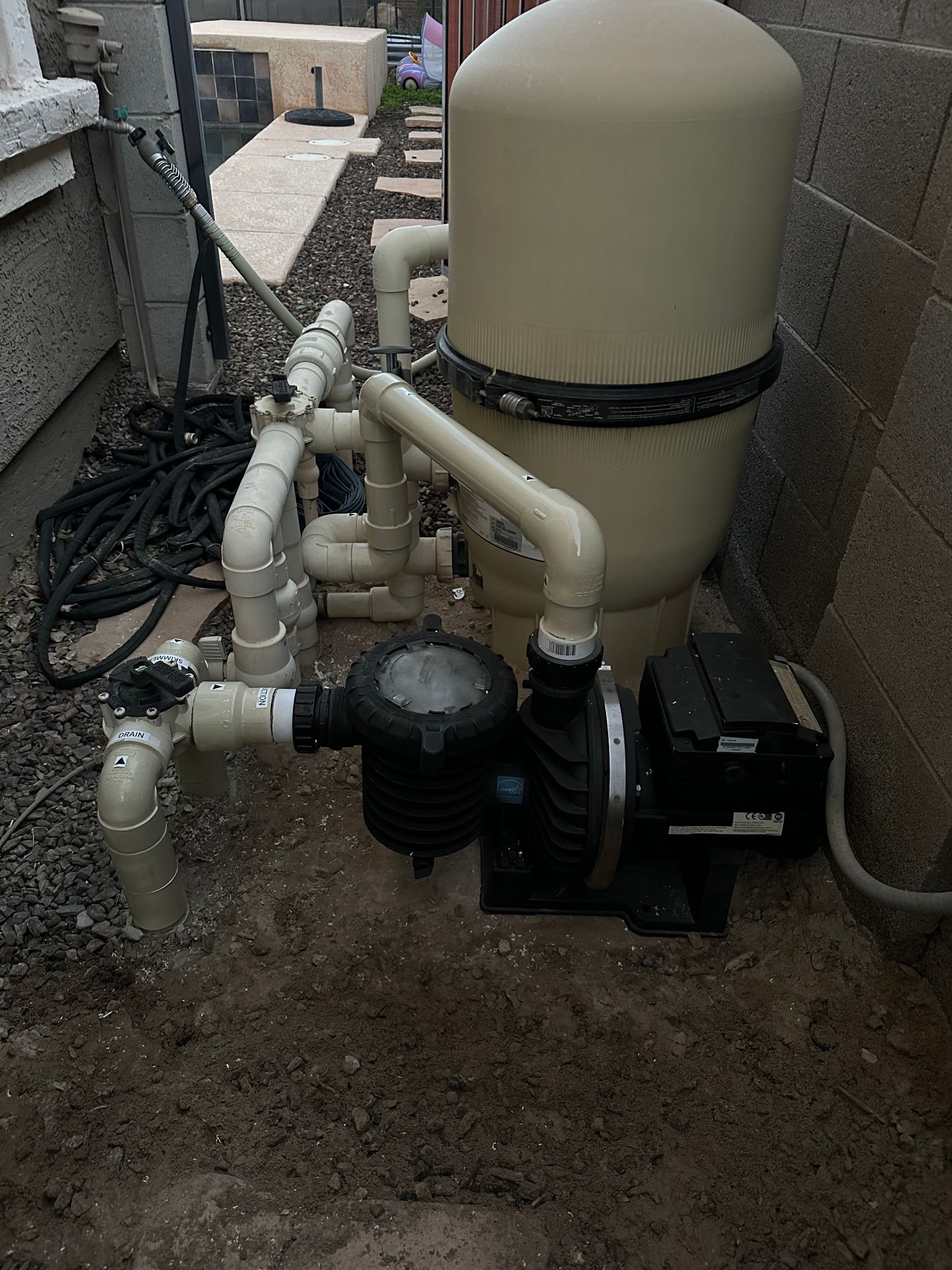 Pool filter system outdoors with a pump, filter tank, and plumbing.
