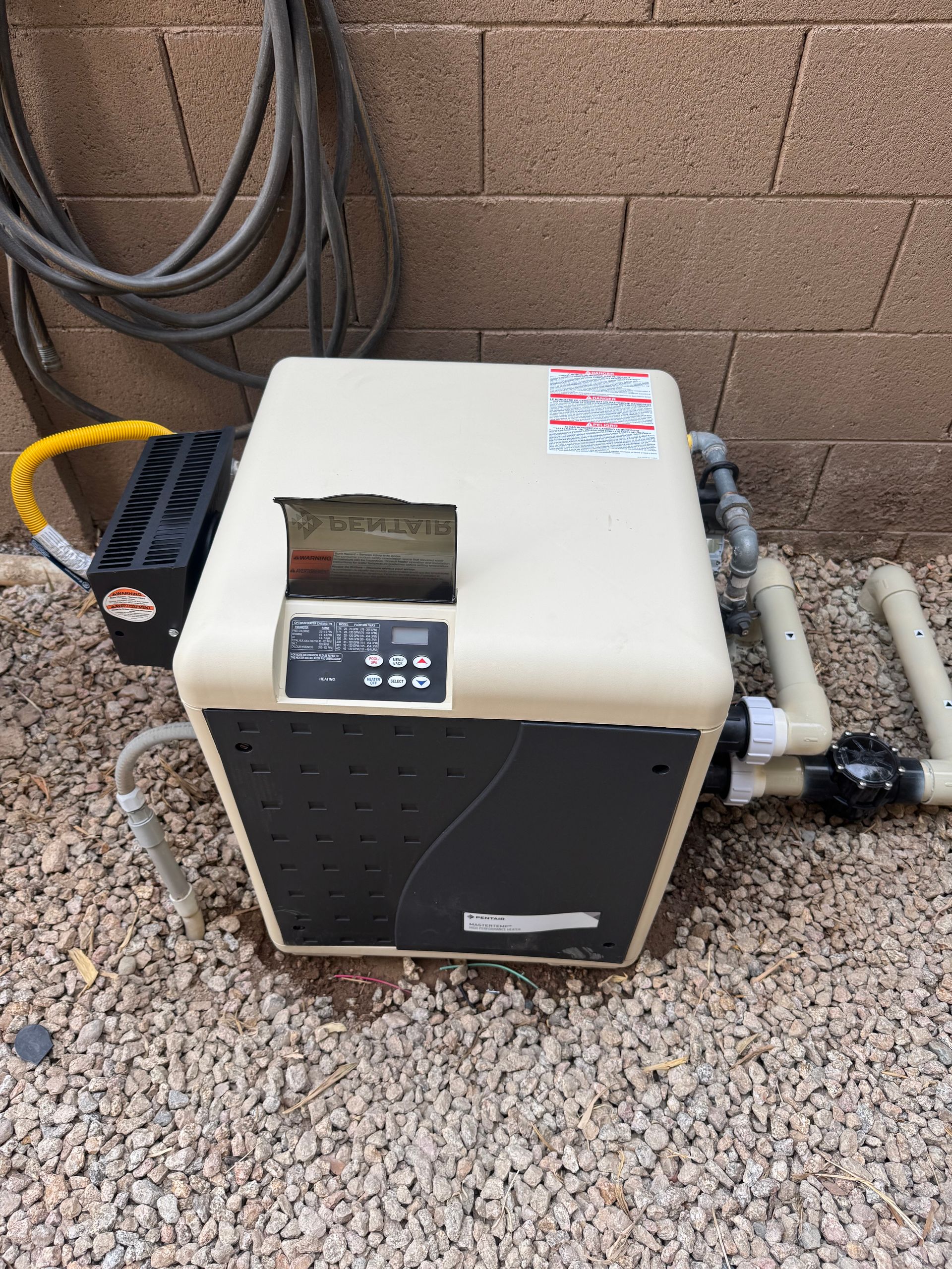 Pool heater with damaged top, on gravel next to a brick wall.