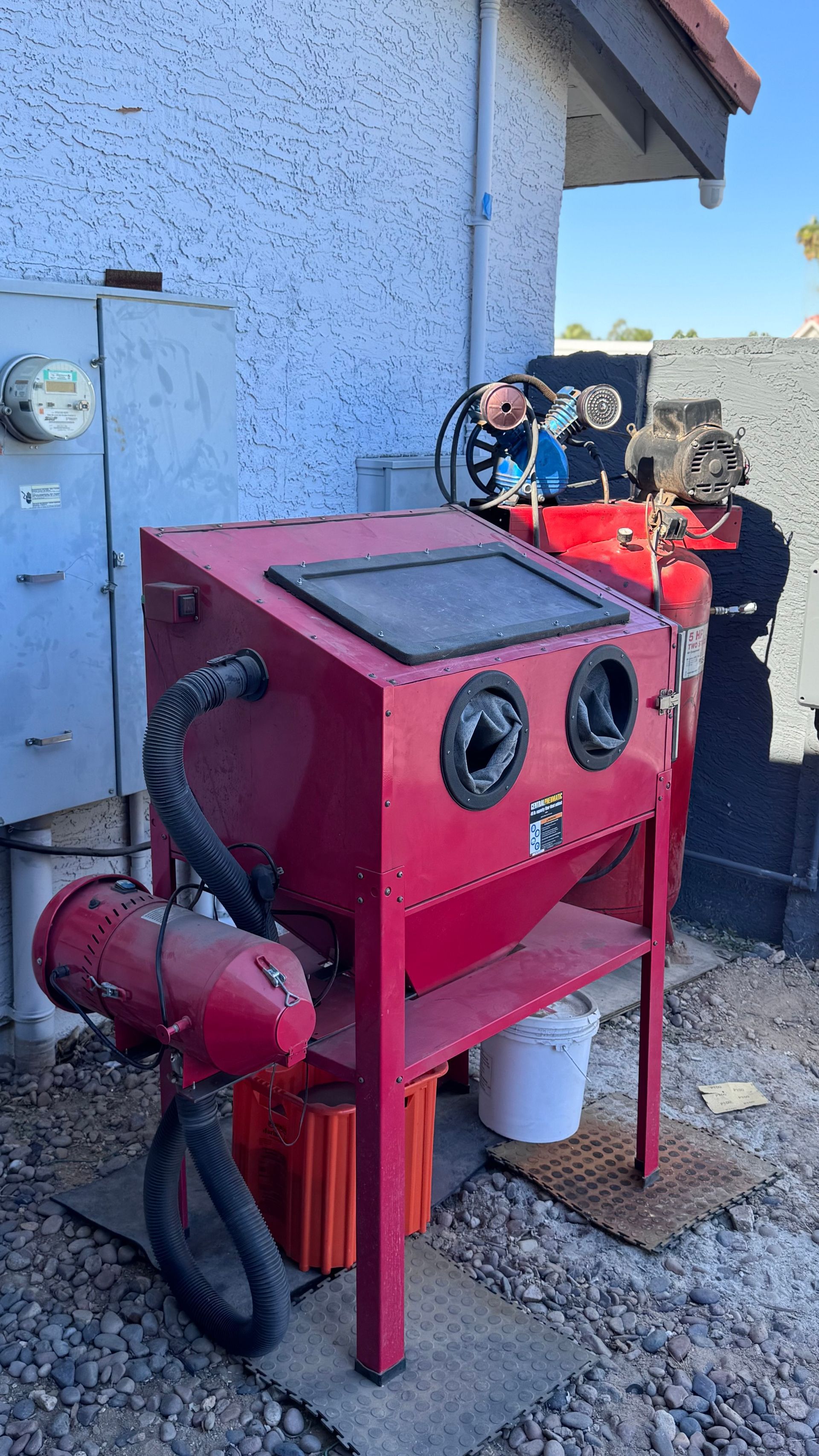Red sandblasting cabinet outdoors with attached equipment.