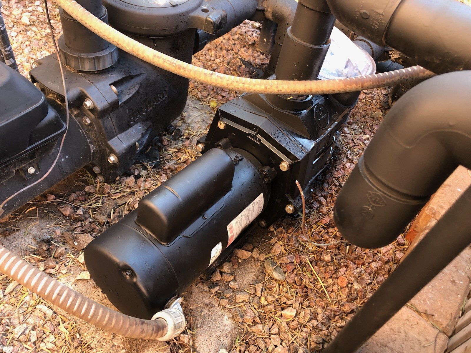 A black pump is sitting on the ground next to pipes.