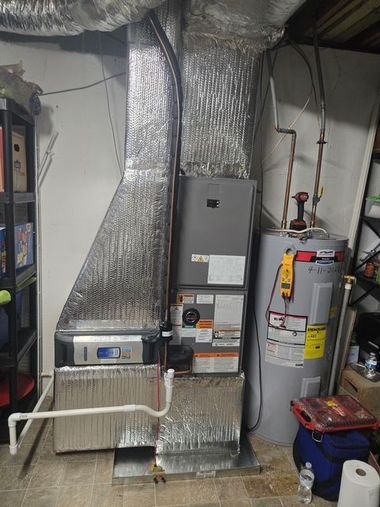 Furnace and water heater in a basement. Metal ducts and insulation visible. Tools are nearby.