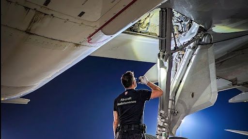A man is working on the underside of an airplane.