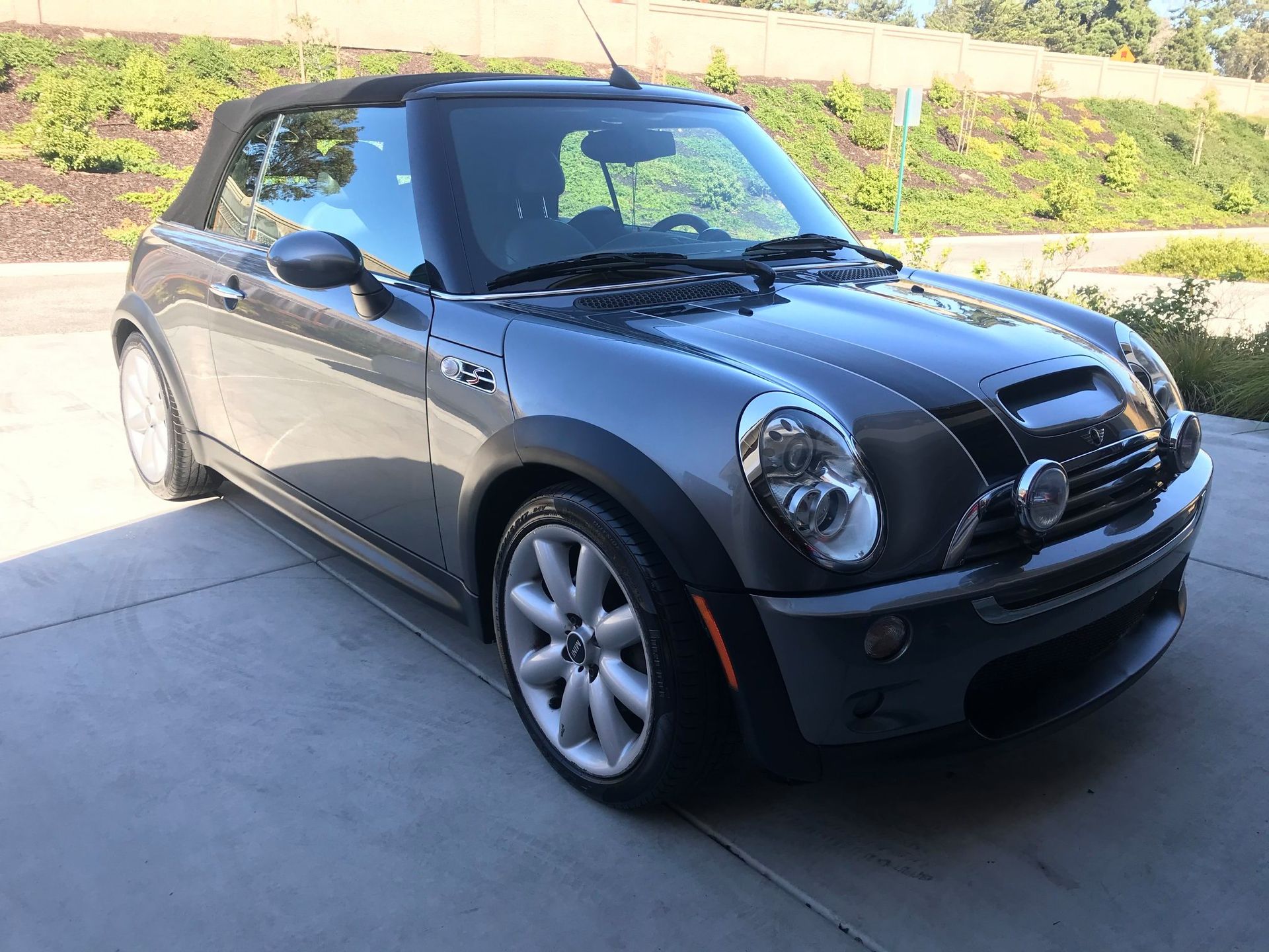 Black Mini Cooper convertible parked in a driveway with the top down.