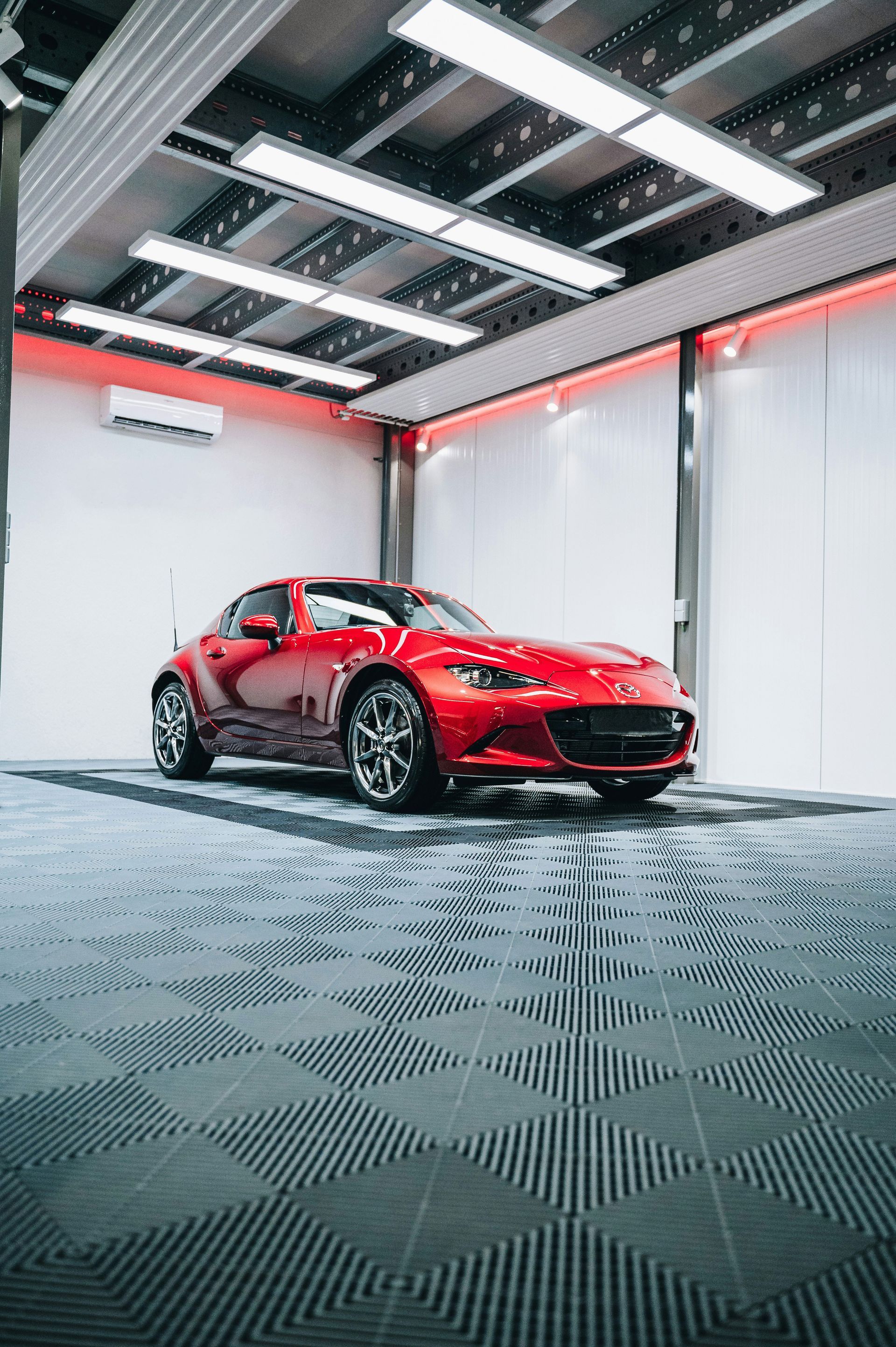Red sports car in a modern garage with overhead lights and patterned floor