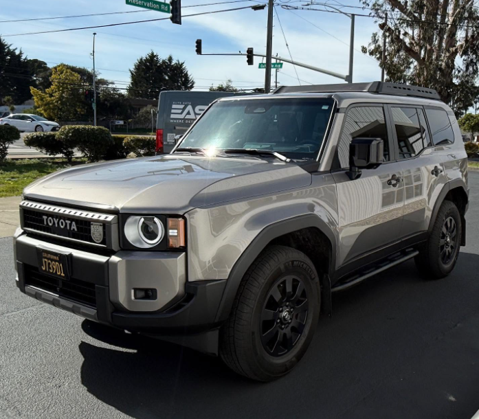 Silver Toyota SUV on a street, front three-quarter view, with a traffic light and truck in the background