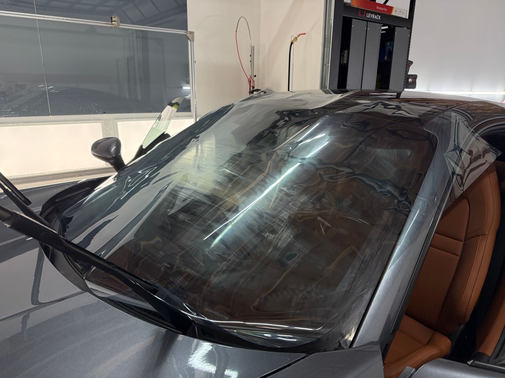 Black car in a garage, with a cracked windshield and tan interior visible