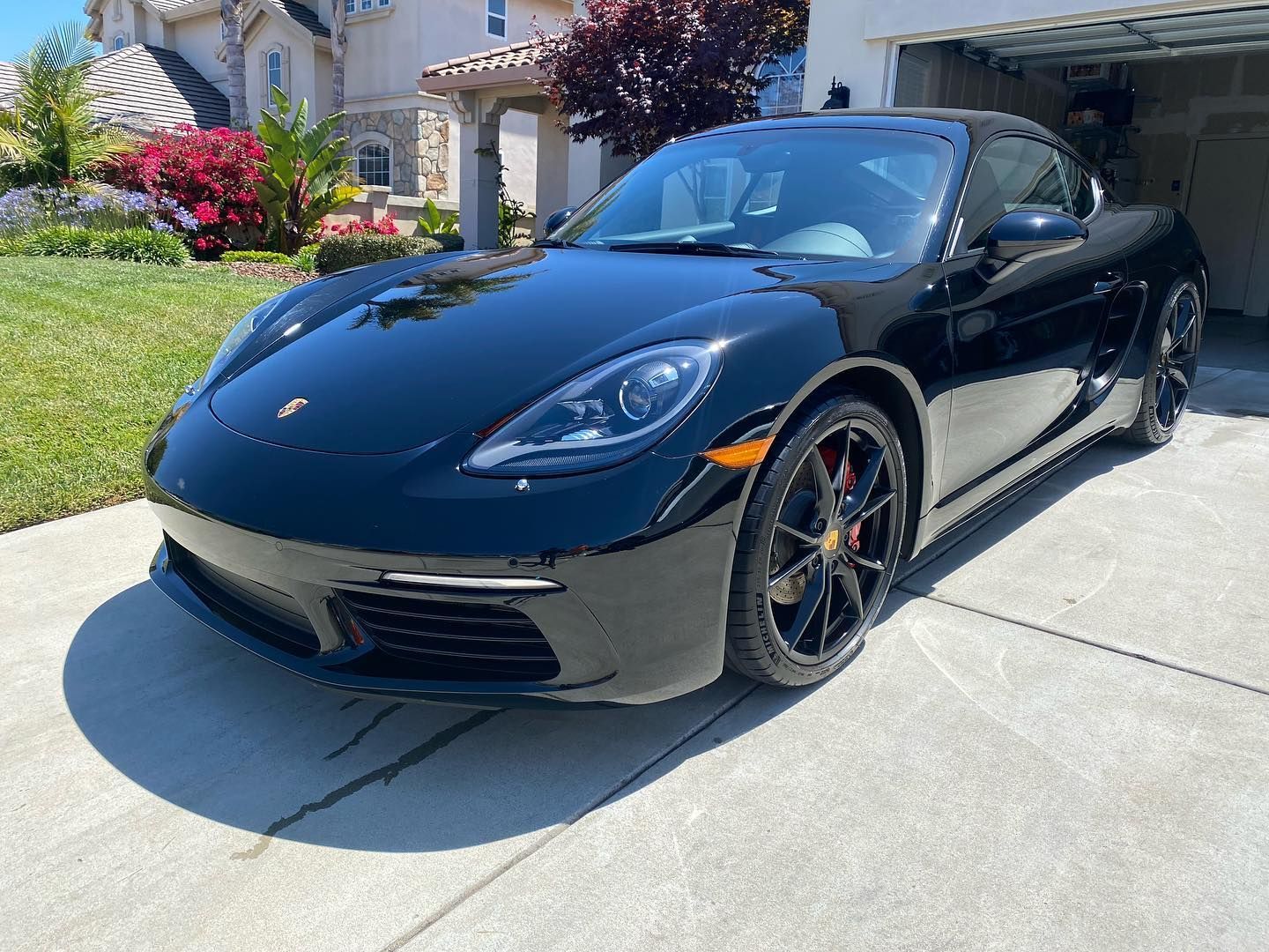 Black Porsche convertible parked in a driveway in front of a house