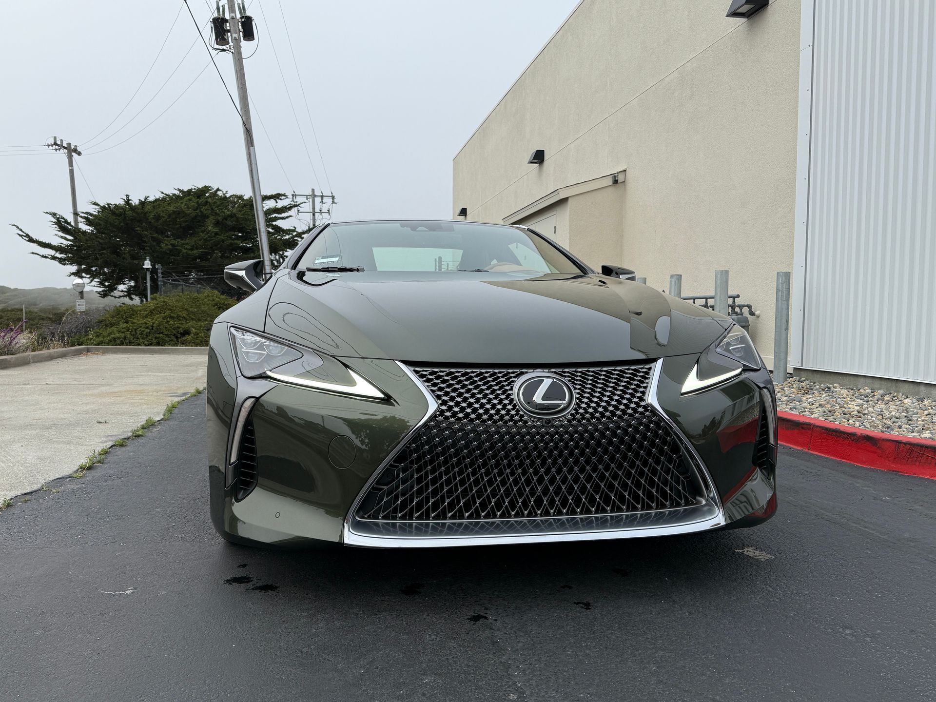 Front view of a black Lexus parked on a street beside a beige building.