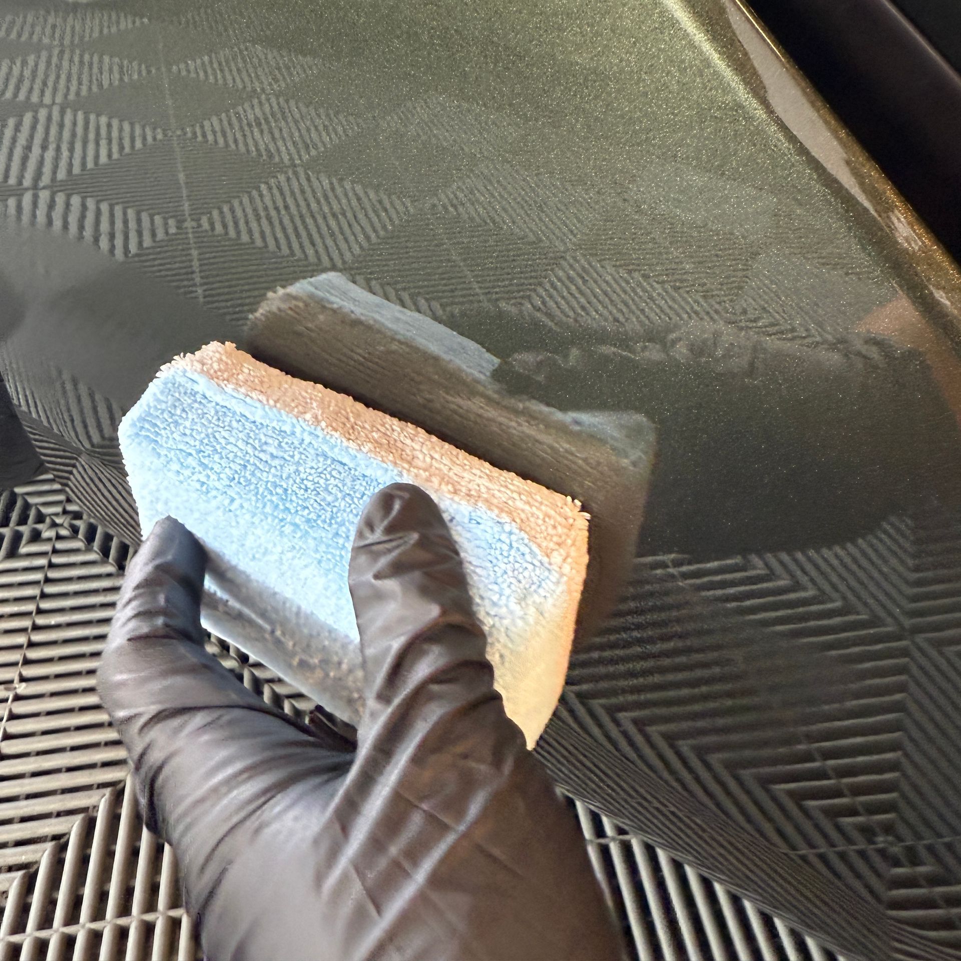 Gloved hand wiping a dark patterned surface with a blue-and-orange sponge