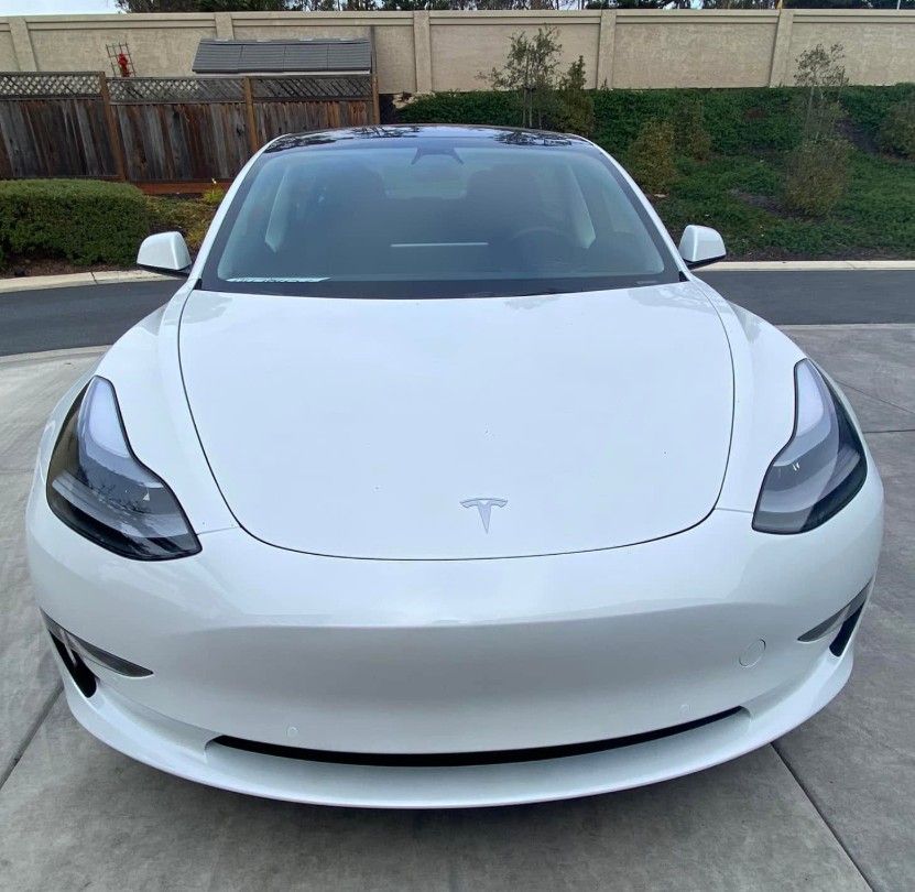 White Tesla sedan parked in a driveway, front view.