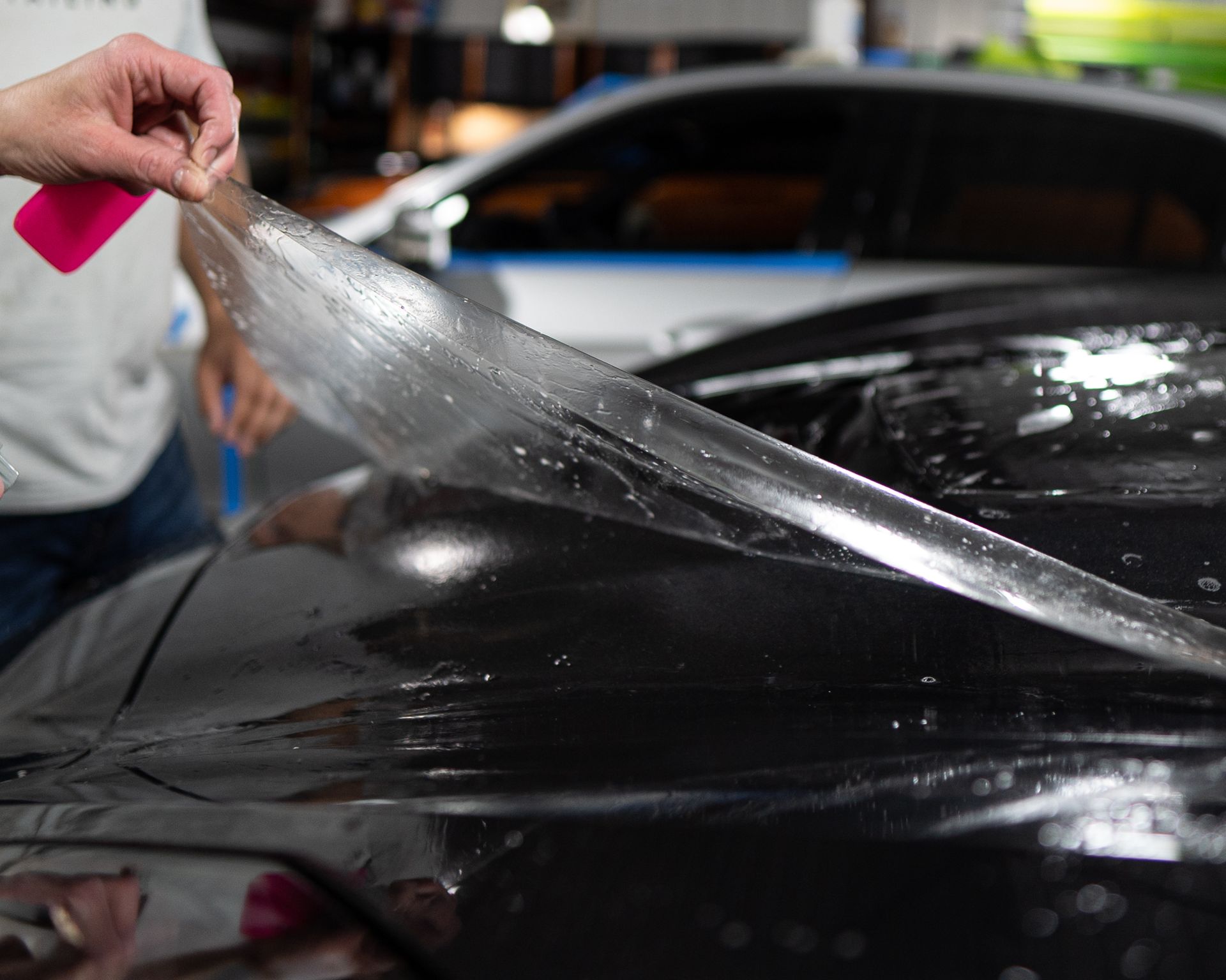 A person is applying a clear film to the hood of a car.
