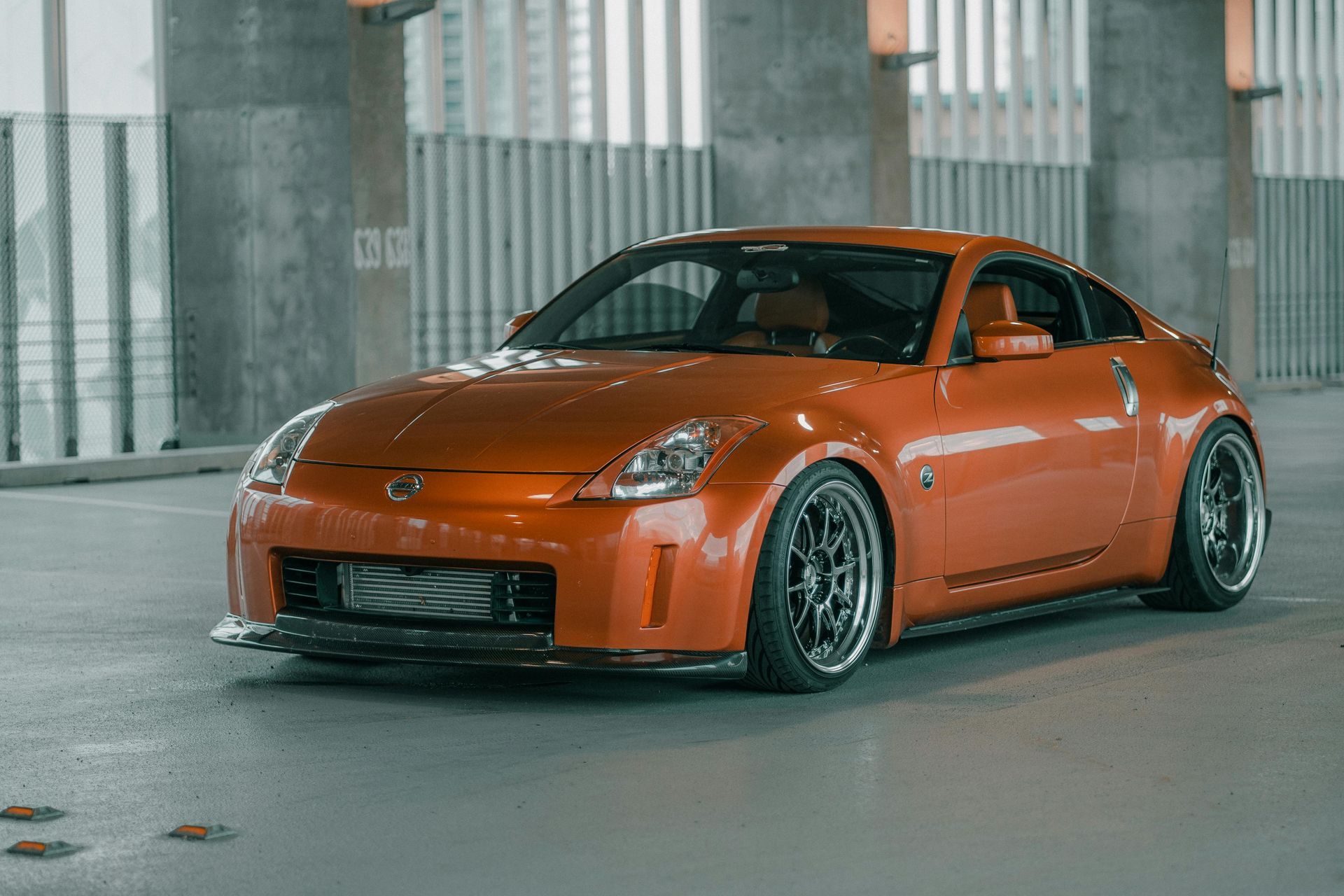 Orange sports coupe parked in a concrete garage, viewed from the front-left side.