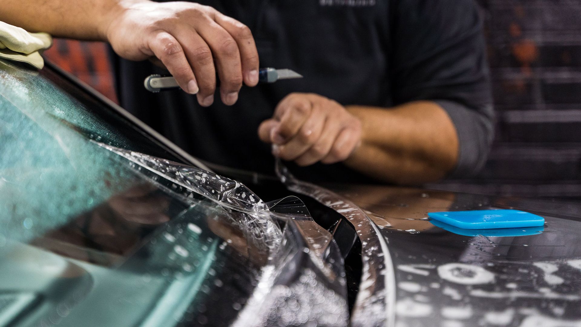 Hands use a suction tool to lift a car windshield in a repair shop