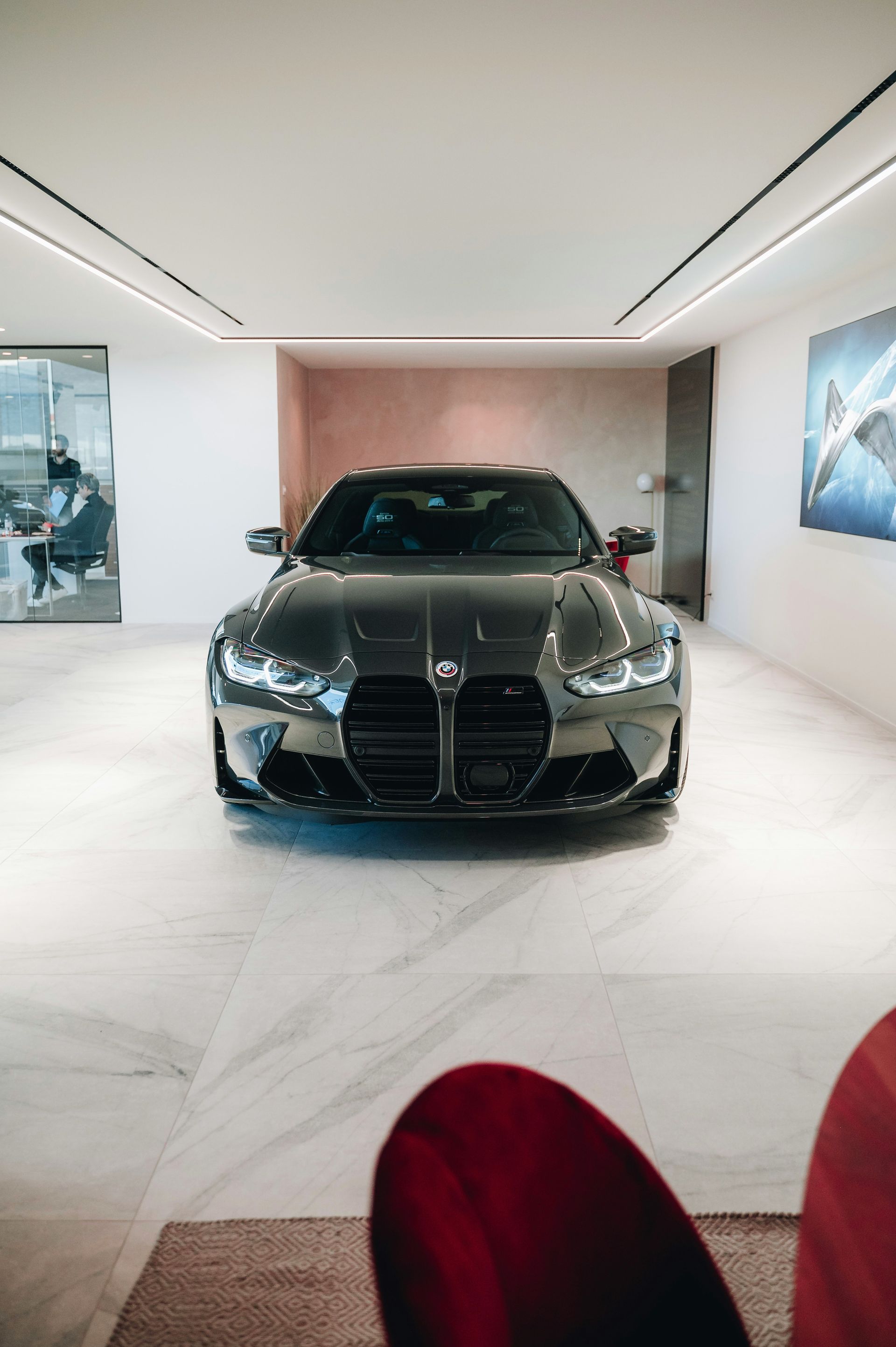 Black luxury sedan displayed in a bright showroom with white floors and wall art.