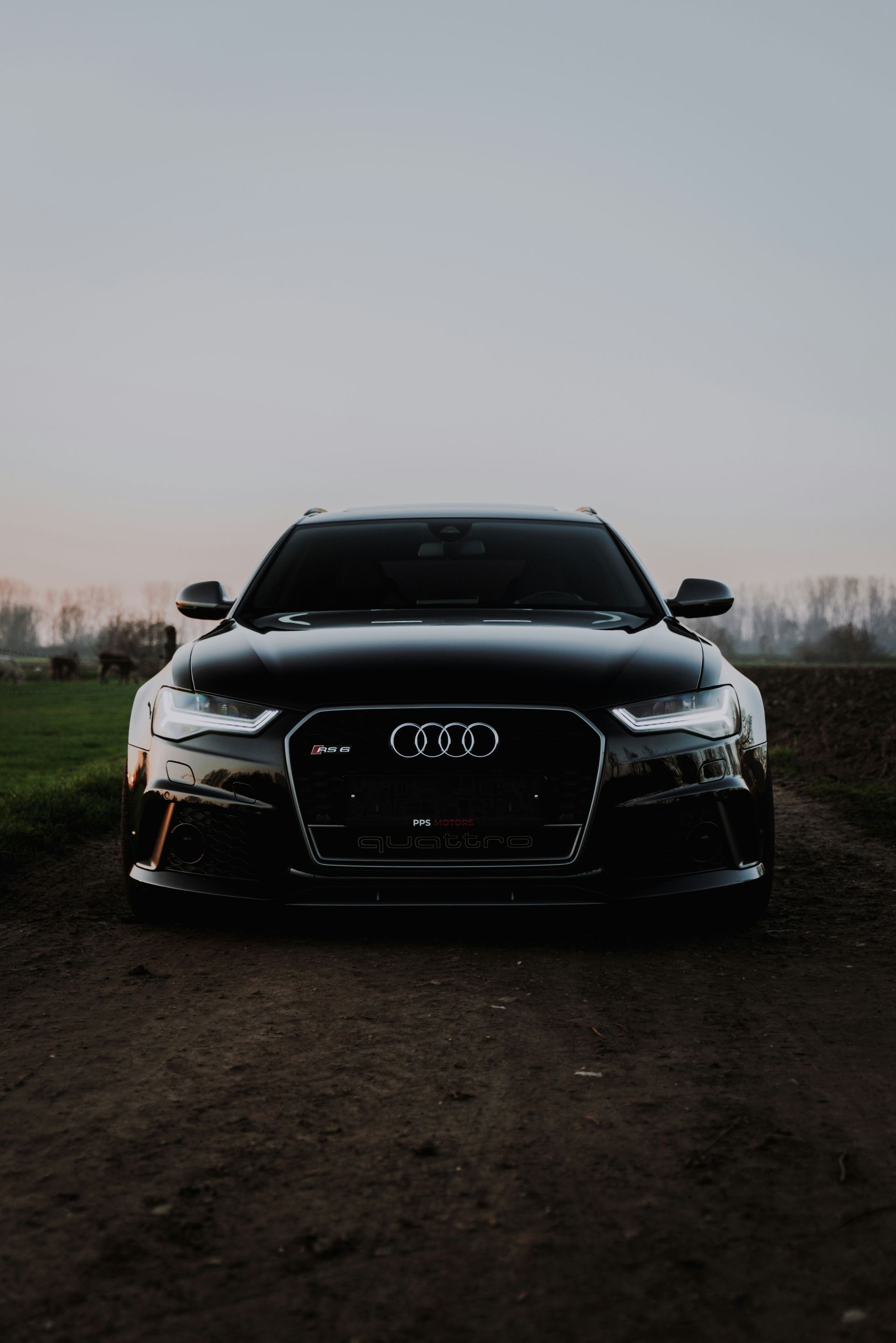 Black Audi car parked on a dirt road at dusk, front view with headlights on