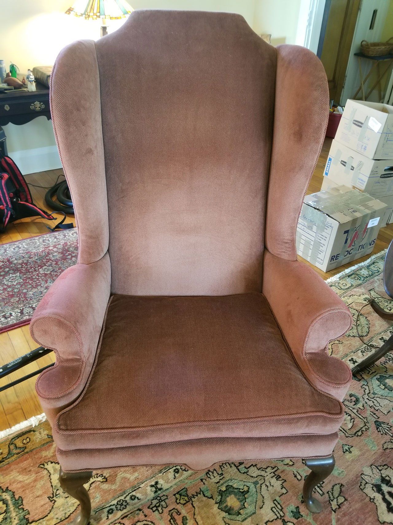 A dusty rose, textured wingback chair stands in a carpeted room with boxes in the background.