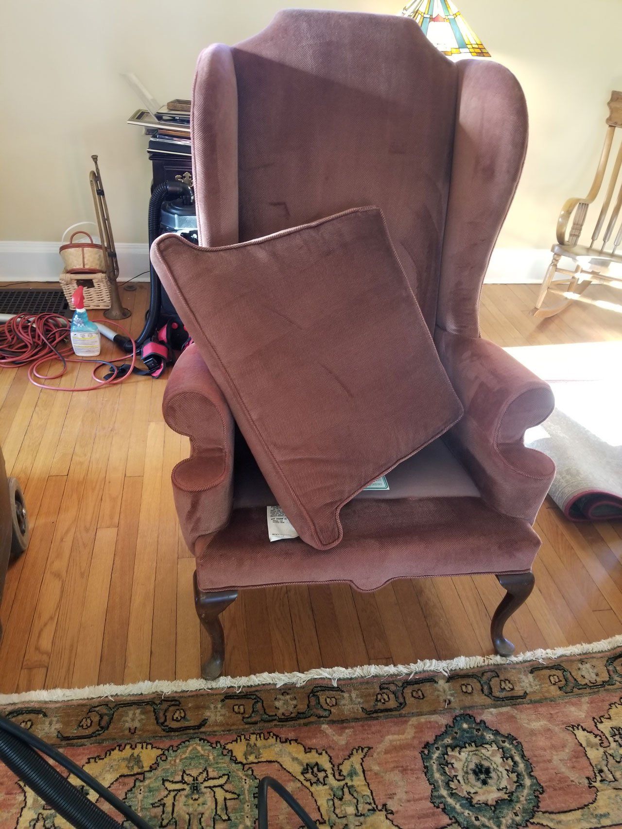 A maroon wingback chair sits on a hardwood floor with its seat cushion resting vertically against the backrest.