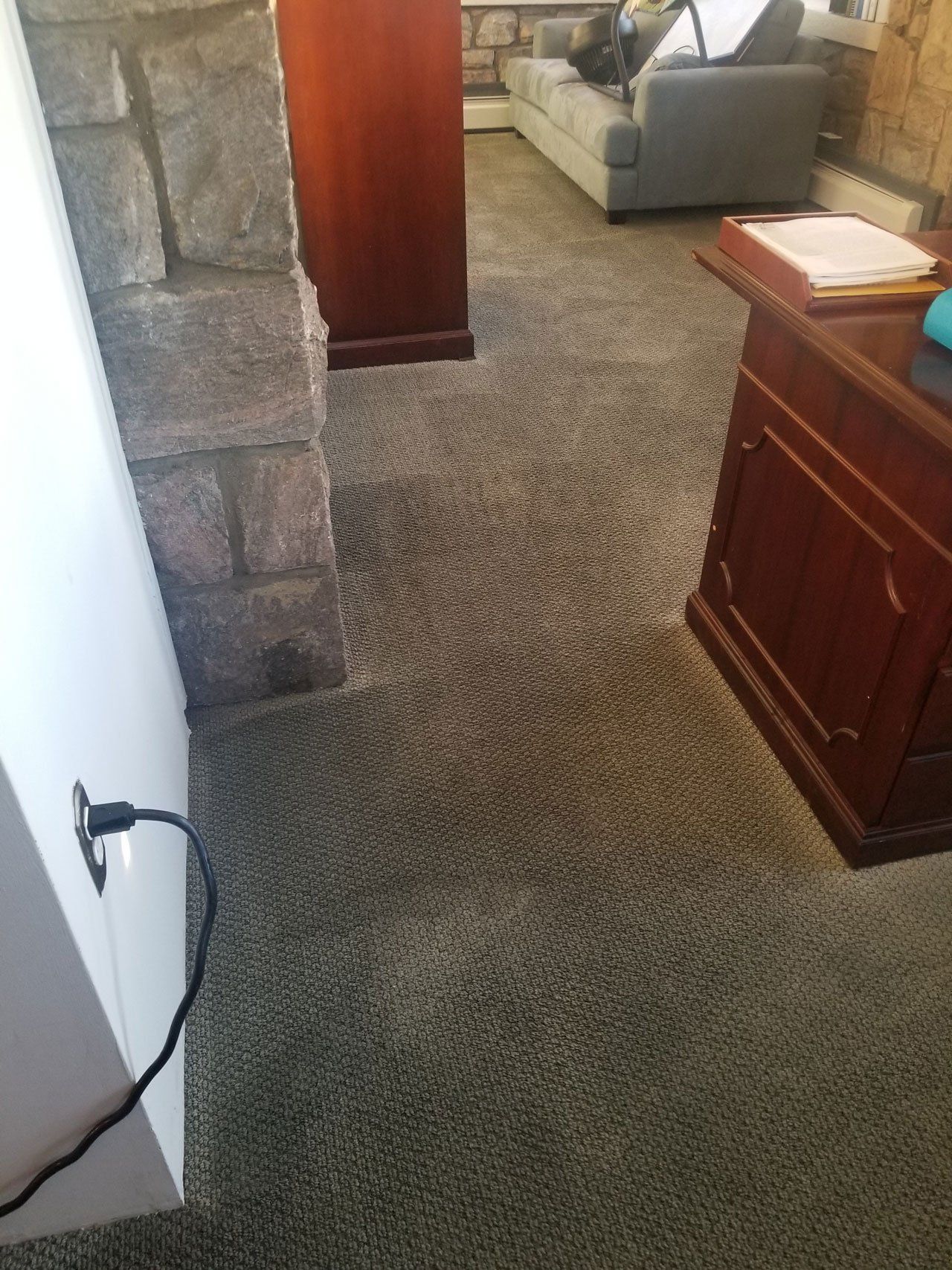 A view of a carpeted room featuring a stone pillar, a wooden desk, and a gray sofa in the background.