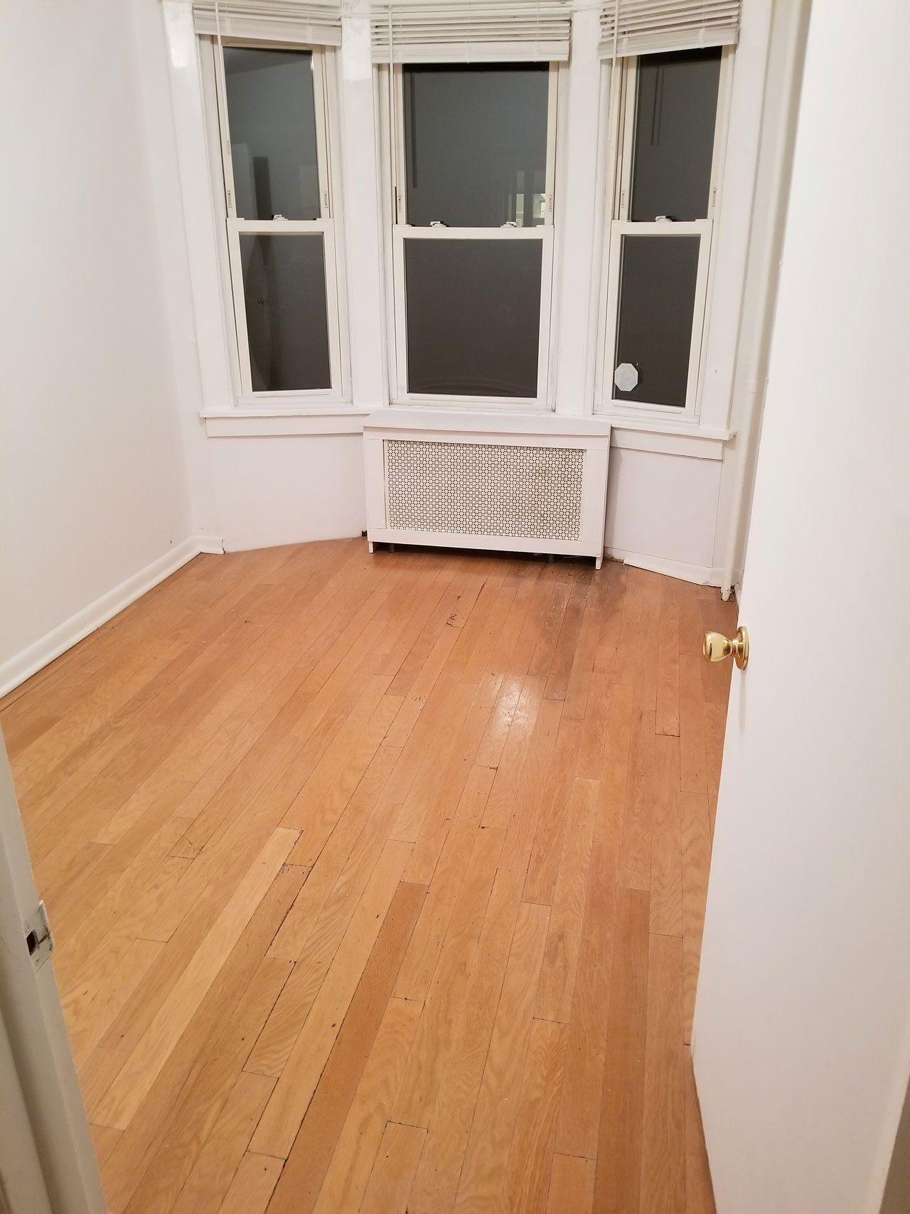 Empty room with light wood floors, white walls, and a bay window featuring a white radiator cover underneath.