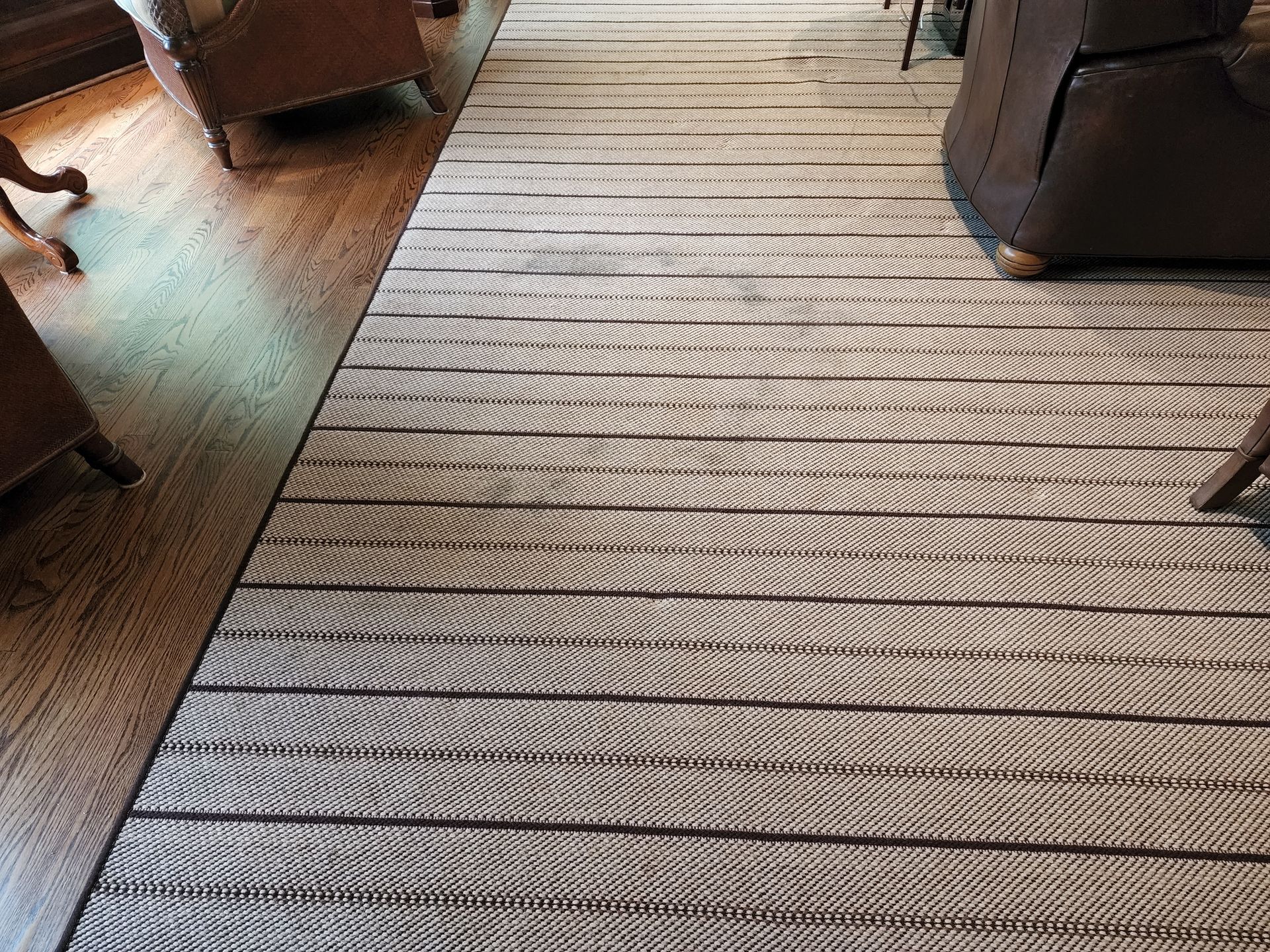 A striped woven rug covers a dark wood floor, flanked by parts of chairs in a dimly lit room.