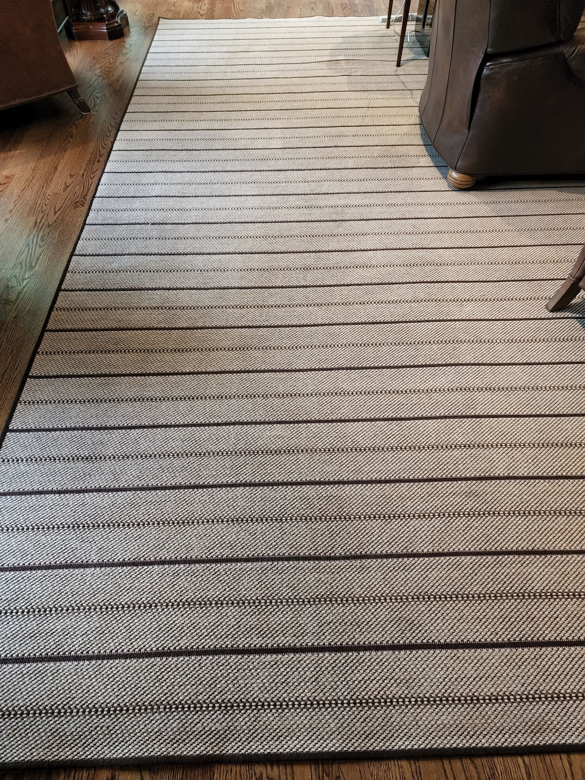 A neutral-toned area rug with a repeating textured horizontal stripe pattern on a wooden floor.