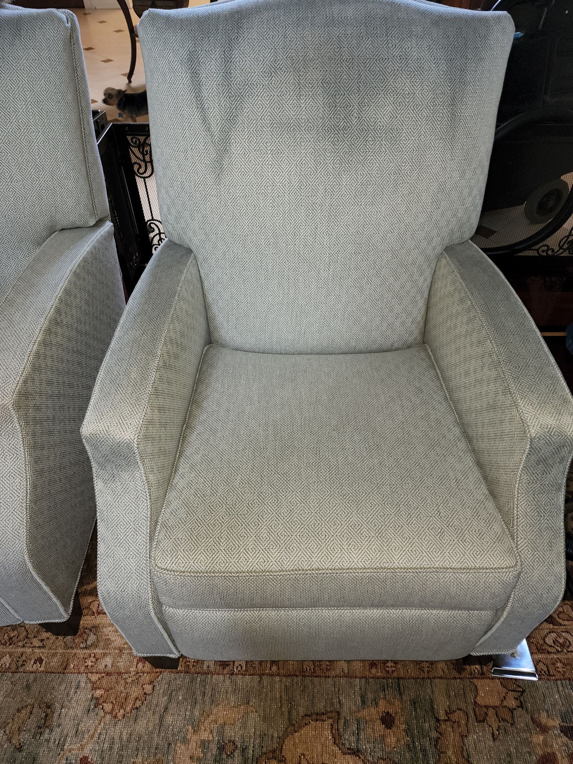 Two matching, light grey patterned armchairs sitting on a speckled carpet.
