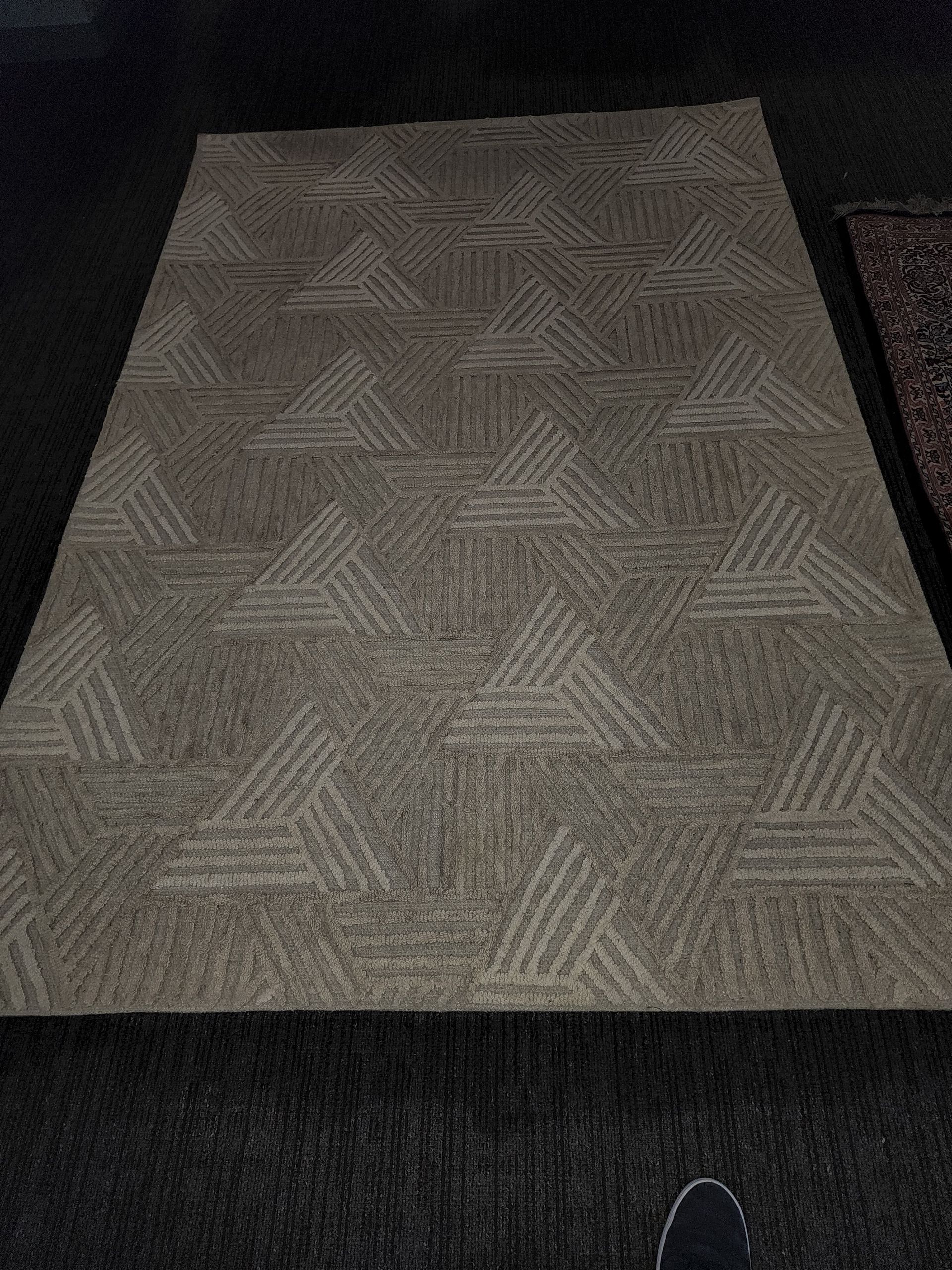 A rectangular area rug in shades of tan and cream with a repeating geometric pattern of triangular motifs.