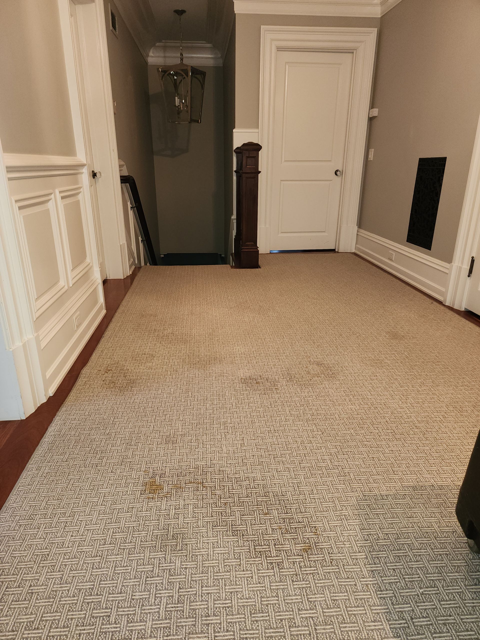 A hallway with textured light-patterned carpet, cream-colored walls with molding, a wooden grandfather clock, and doorways.