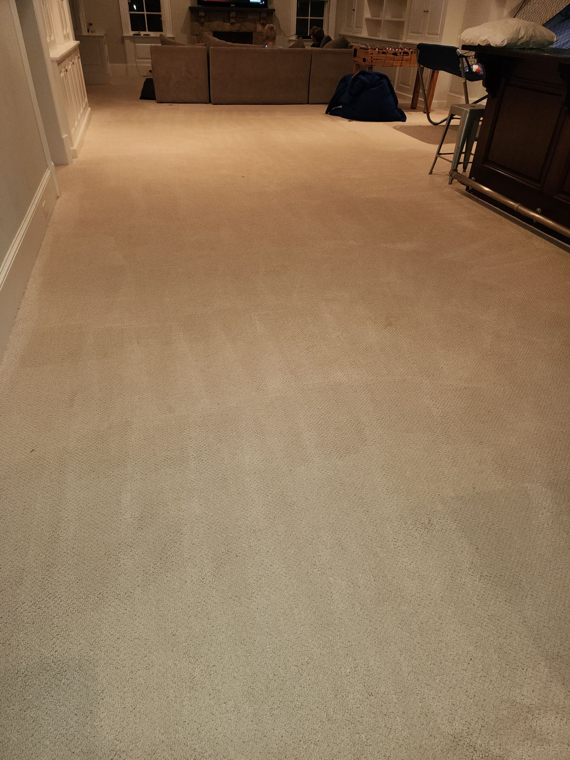 A beige carpet covers a hallway leading toward an open living area with a couch and bar-style table.